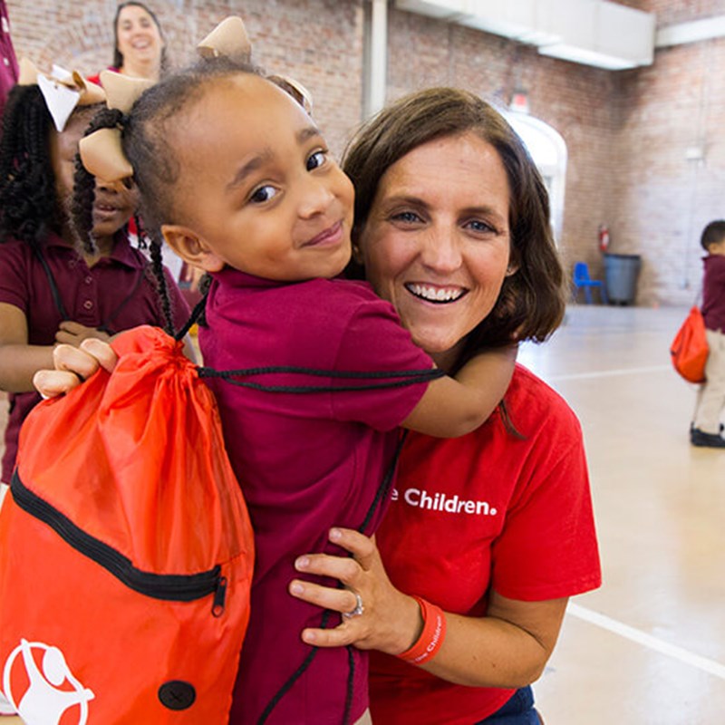 Young girl with a backpack hugging a volunteer